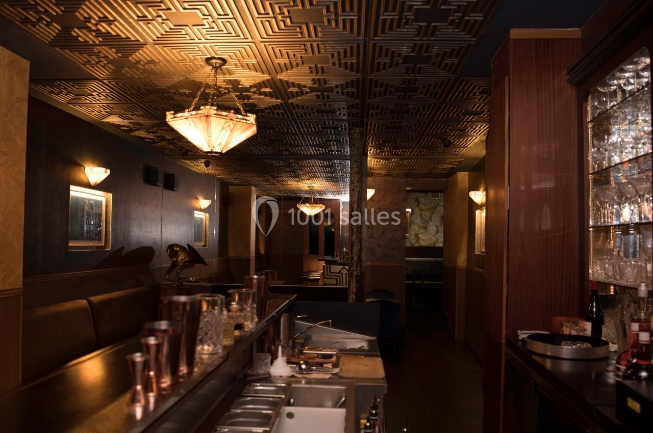 Intérieur d'un bar avec un comptoir en premier plan, un plafond décoratif et un éclairage tamisé.