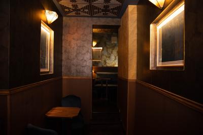 Une main tenant un verre de vin blanc dans un environnement sombre, avec des personnes et une lampe en arrière-plan.