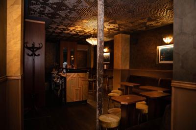 Une main tenant un verre de vin blanc dans un environnement sombre, avec des personnes et une lampe en arrière-plan.