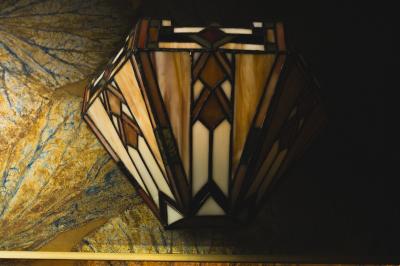 Une main tenant un verre de vin blanc dans un environnement sombre, avec des personnes et une lampe en arrière-plan.