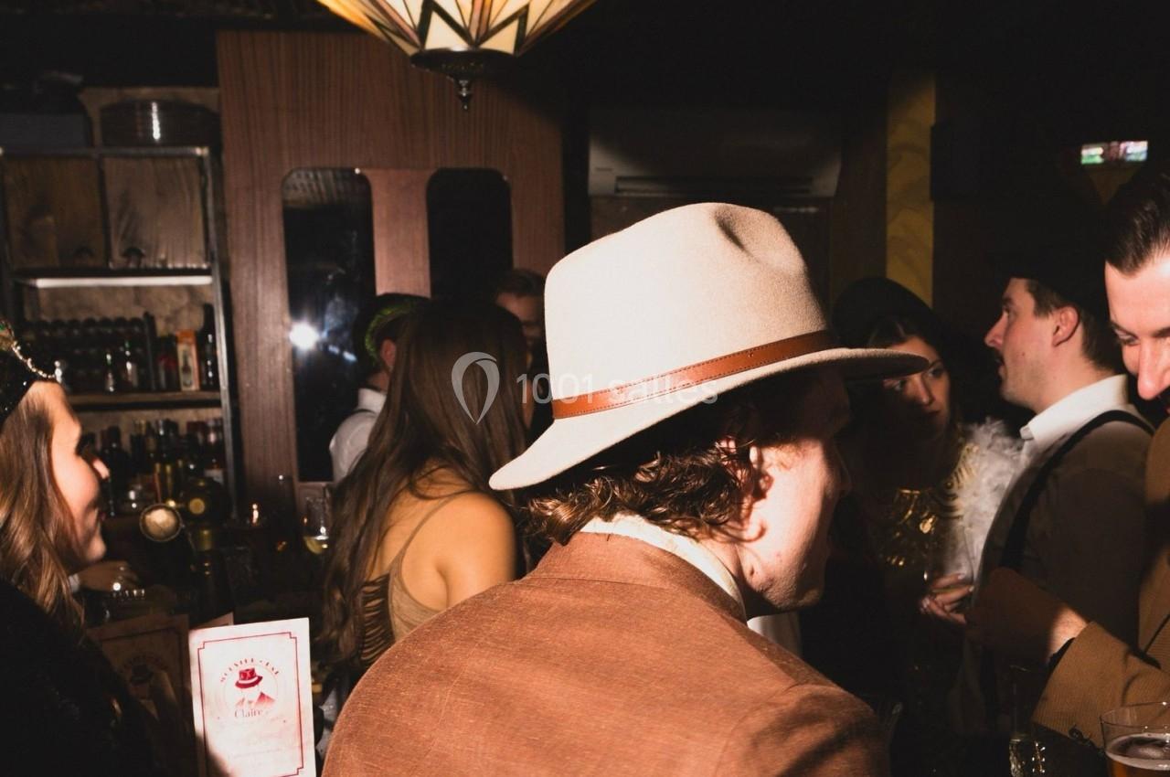 Personnes discutant dans un bar ou une soirée, ambiance tamisée avec décor rétro et lumières chaudes.