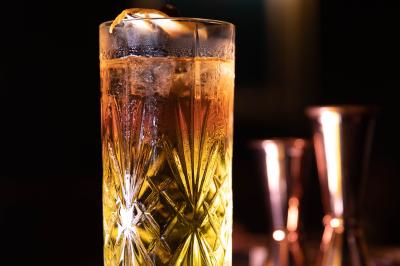Une femme assise dans un bar sombre tient un menu près d'un cocktail rouge servi dans un verre élégant.