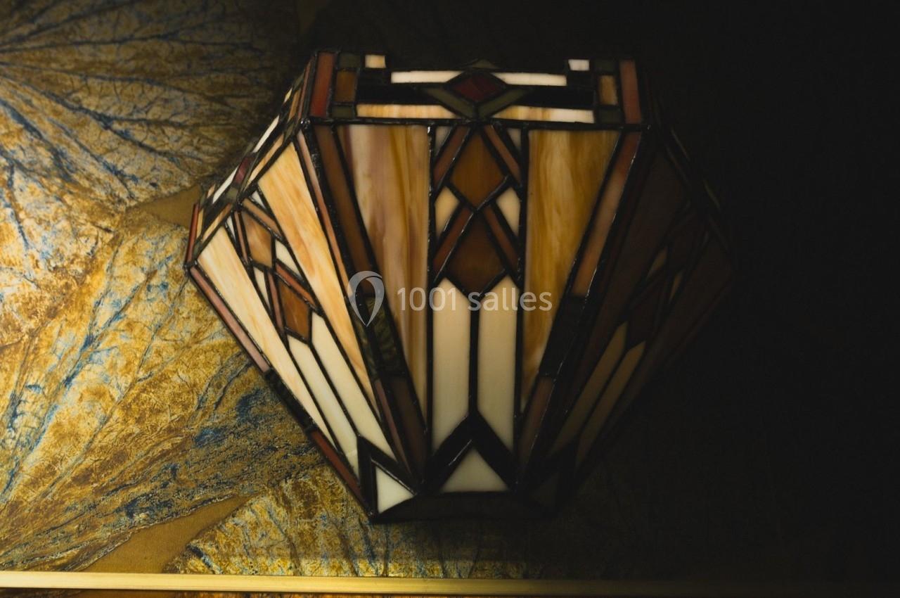 Lampe en vitrail coloré de style art déco, posée sur une surface texturée aux tons dorés et bleus.