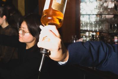 Une femme assise dans un bar sombre tient un menu près d'un cocktail rouge servi dans un verre élégant.