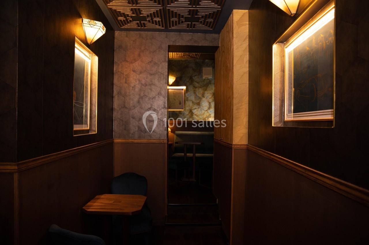 Intérieur d'un espace sombre avec des murs texturés, des appliques lumineuses et des tables en bois.