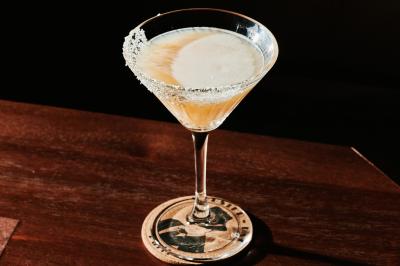 Une femme assise dans un bar sombre tient un menu près d'un cocktail rouge servi dans un verre élégant.