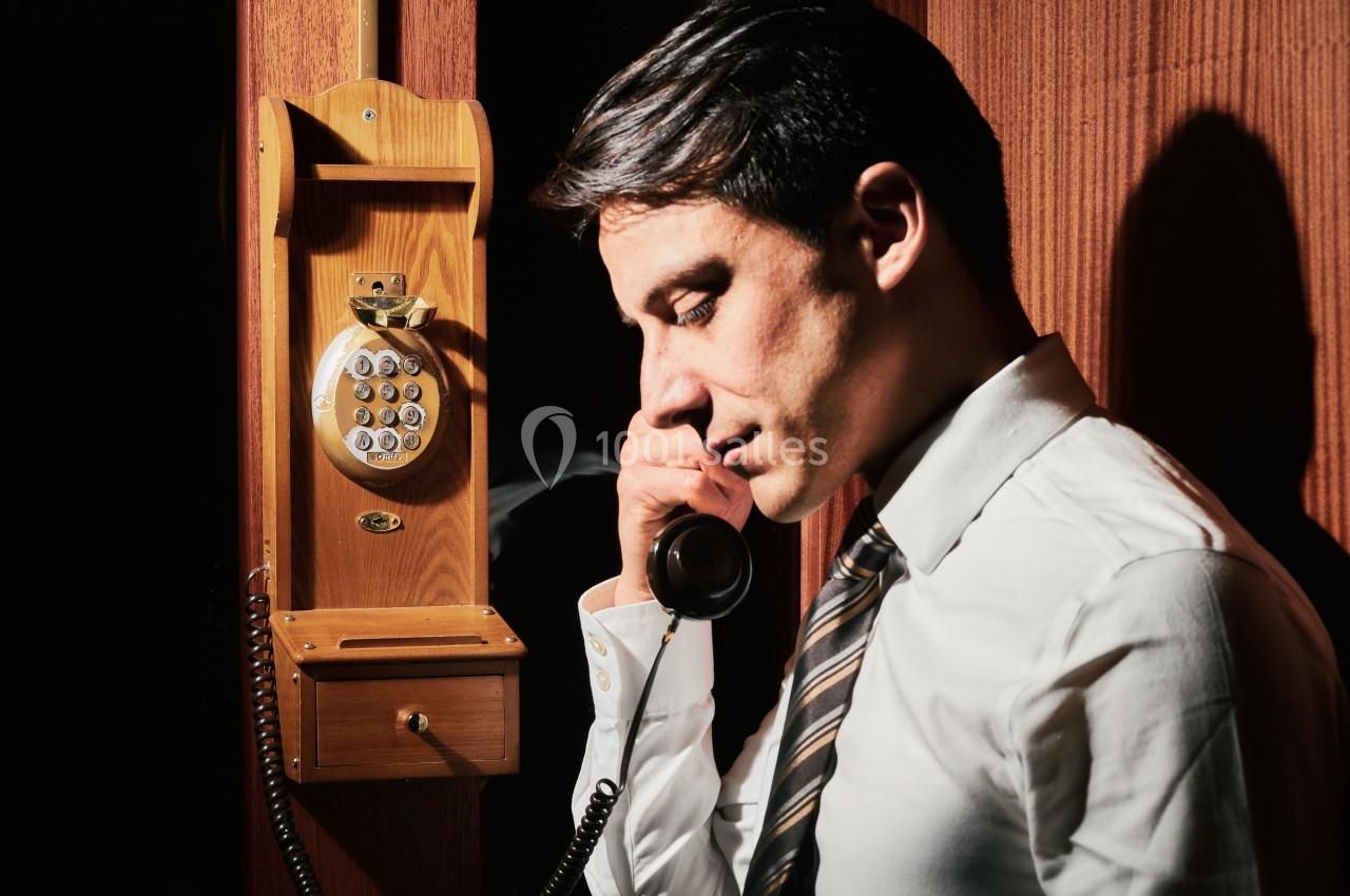 Homme en chemise blanche utilisant un téléphone fixe vintage en bois, éclairé par une lumière directe.