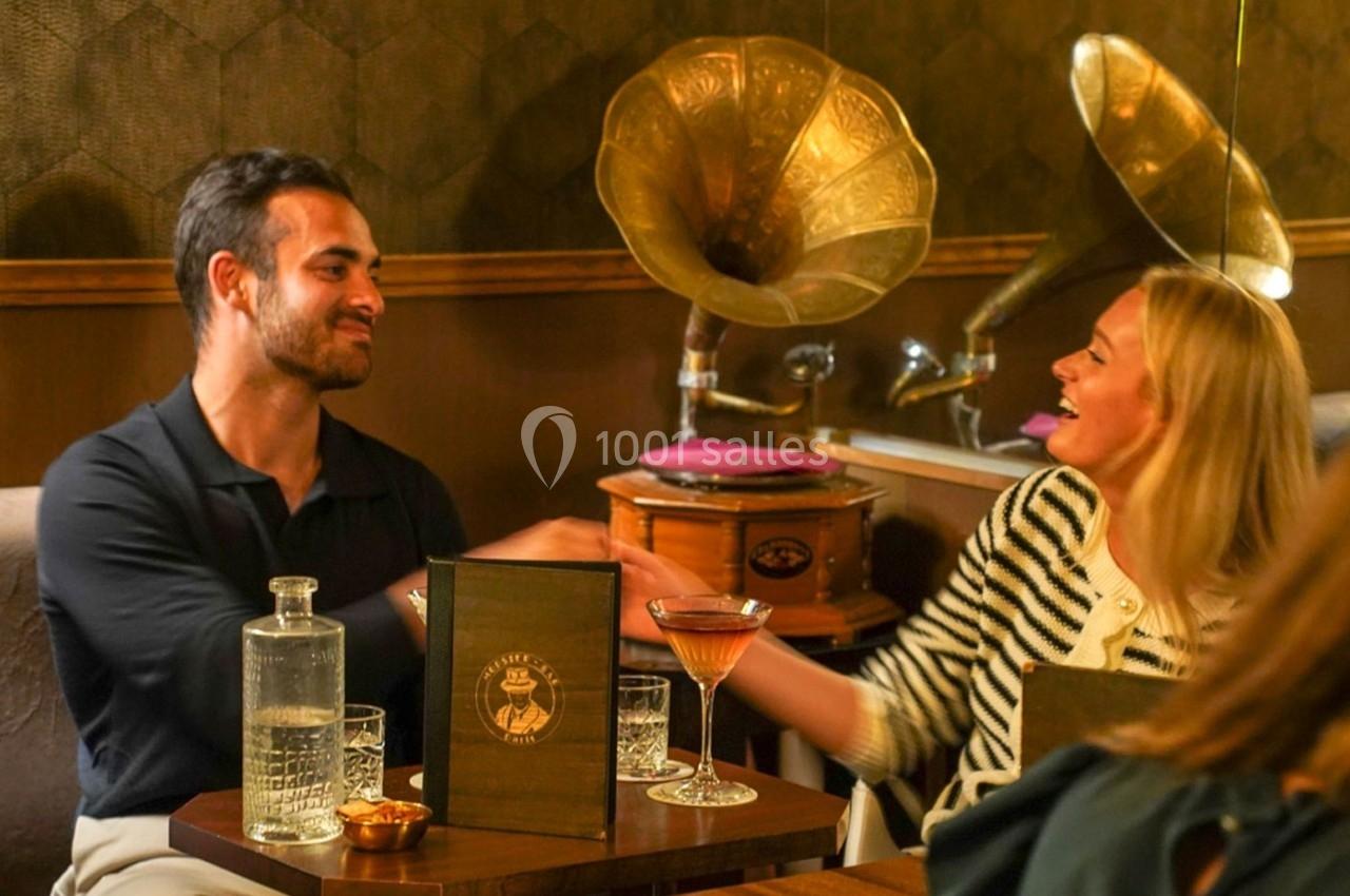Un homme et une femme sourient et se serrent la main dans un café rétro avec des gramophones en arrière-plan.