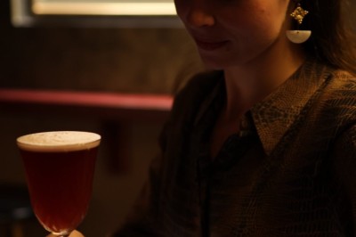 Une femme assise dans un bar sombre tient un menu près d'un cocktail rouge servi dans un verre élégant.
