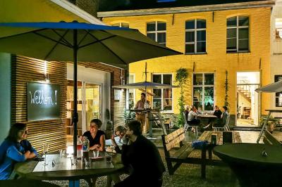 Salle élégante avec parquet, comptoir noir, lustre central et grandes fenêtres encadrées de rideaux.