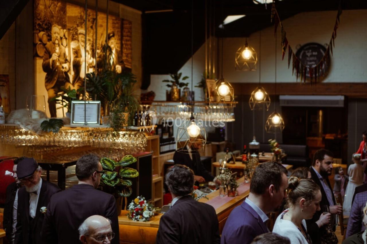 Un bar animé avec des clients discutant, des luminaires suspendus et une décoration chaleureuse en arrière-plan.