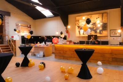 Salle élégante avec parquet, comptoir noir, lustre central et grandes fenêtres encadrées de rideaux.