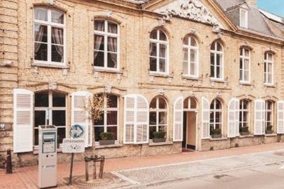 Salle élégante avec parquet, comptoir noir, lustre central et grandes fenêtres encadrées de rideaux.
