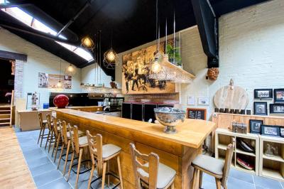 Salle élégante avec parquet, comptoir noir, lustre central et grandes fenêtres encadrées de rideaux.