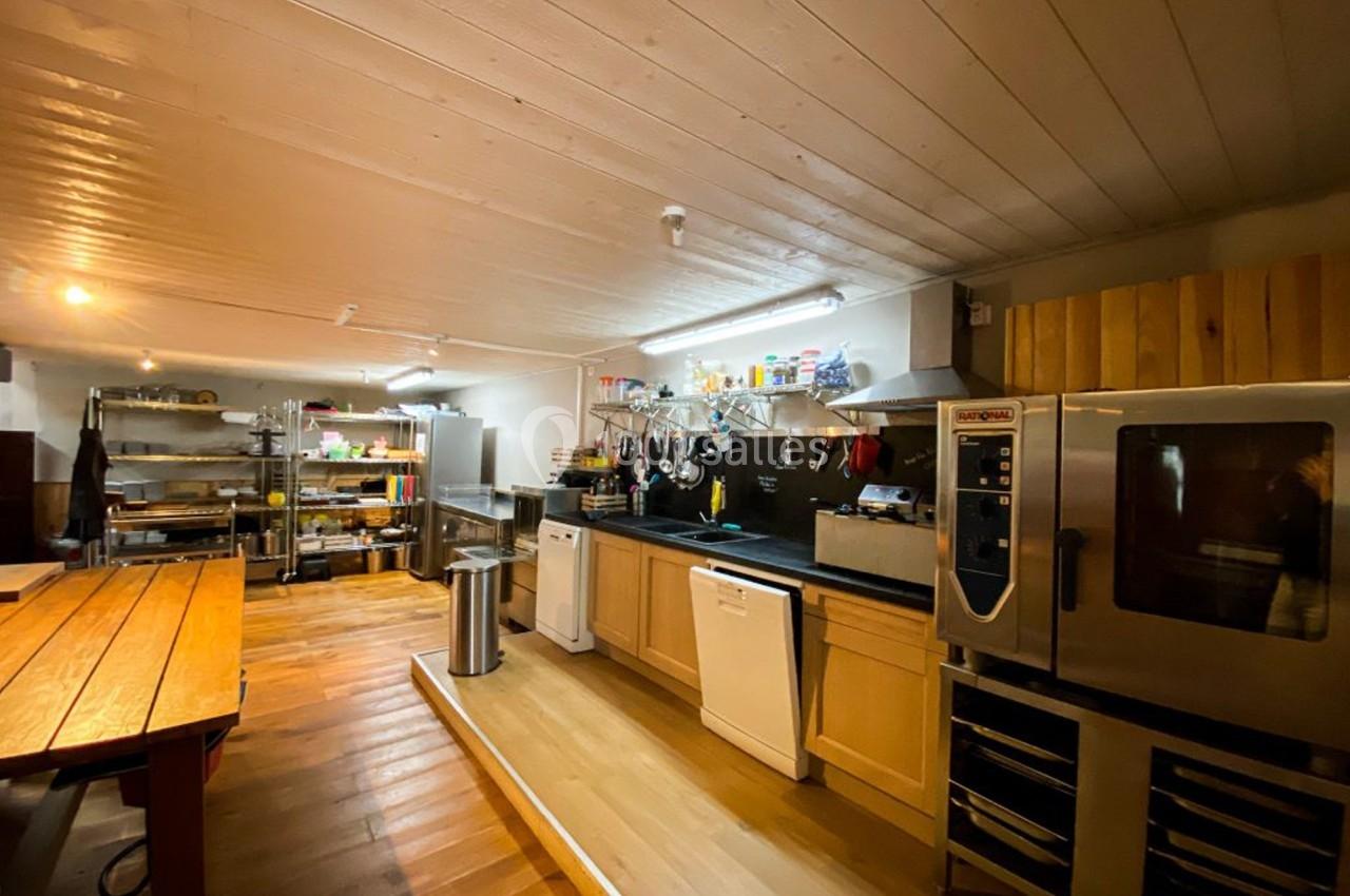 Cuisine professionnelle avec plan de travail, étagères de rangement, four industriel et éclairage chaleureux.