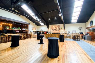 Salle élégante avec parquet, comptoir noir, lustre central et grandes fenêtres encadrées de rideaux.