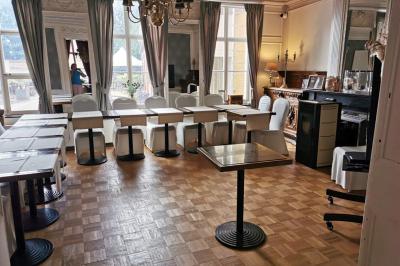Salle élégante avec parquet, comptoir noir, lustre central et grandes fenêtres encadrées de rideaux.