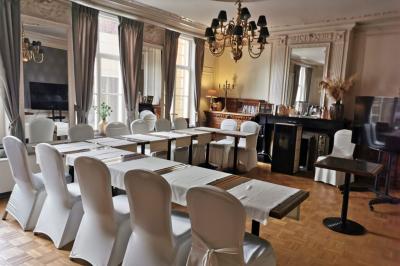 Salle élégante avec parquet, comptoir noir, lustre central et grandes fenêtres encadrées de rideaux.