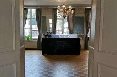 Salle élégante avec parquet, comptoir noir, lustre central et grandes fenêtres encadrées de rideaux.