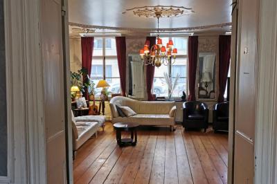 Salle élégante avec parquet, comptoir noir, lustre central et grandes fenêtres encadrées de rideaux.