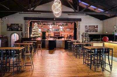Salle élégante avec parquet, comptoir noir, lustre central et grandes fenêtres encadrées de rideaux.