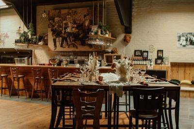 Salle élégante avec parquet, comptoir noir, lustre central et grandes fenêtres encadrées de rideaux.