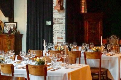 Salle élégante avec parquet, comptoir noir, lustre central et grandes fenêtres encadrées de rideaux.