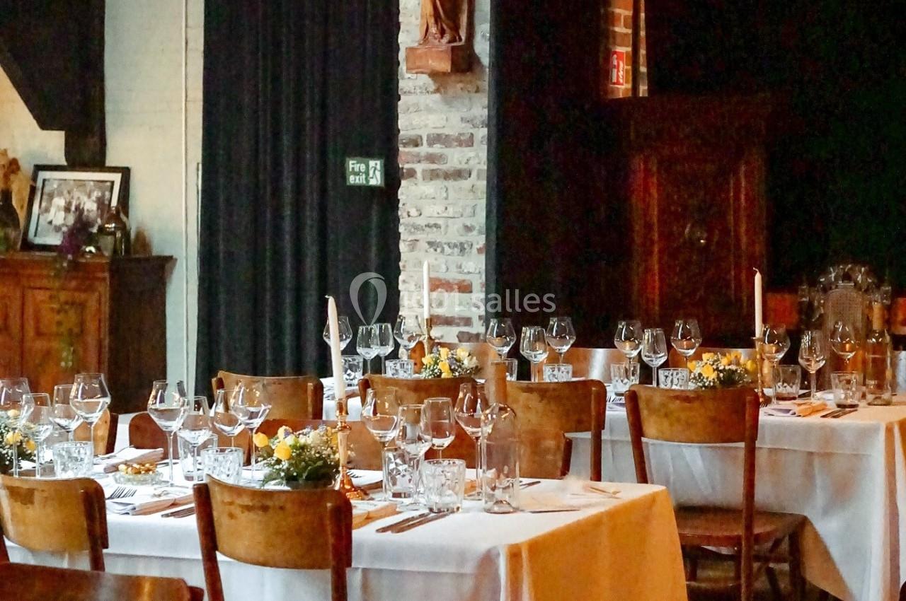 Salle de restaurant avec tables dressées, nappes blanches, verres et décorations, dans un cadre chaleureux en bois et…