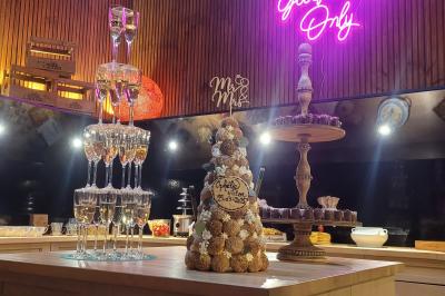 Salle élégante avec parquet, comptoir noir, lustre central et grandes fenêtres encadrées de rideaux.