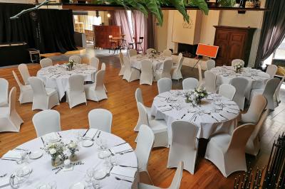Salle élégante avec parquet, comptoir noir, lustre central et grandes fenêtres encadrées de rideaux.