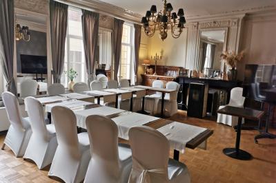 Salle élégante avec parquet, comptoir noir, lustre central et grandes fenêtres encadrées de rideaux.