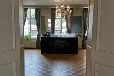 Salle élégante avec parquet, comptoir noir, lustre central et grandes fenêtres encadrées de rideaux.