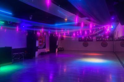 Salle vide avec un sol en parquet sombre, éclairée par la lumière naturelle entrant par de grandes fenêtres.