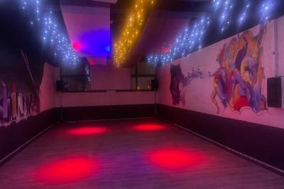 Salle vide avec un sol en parquet sombre, éclairée par la lumière naturelle entrant par de grandes fenêtres.