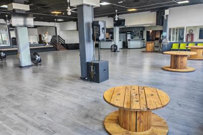 Salle vide avec un sol en parquet sombre, éclairée par la lumière naturelle entrant par de grandes fenêtres.