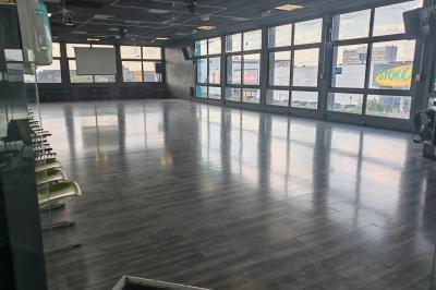 Salle vide avec un sol en parquet sombre, éclairée par la lumière naturelle entrant par de grandes fenêtres.