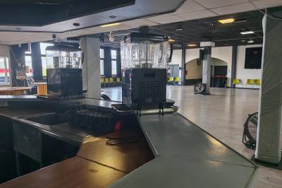 Salle vide avec un sol en parquet sombre, éclairée par la lumière naturelle entrant par de grandes fenêtres.