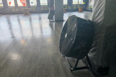 Salle vide avec un sol en parquet sombre, éclairée par la lumière naturelle entrant par de grandes fenêtres.