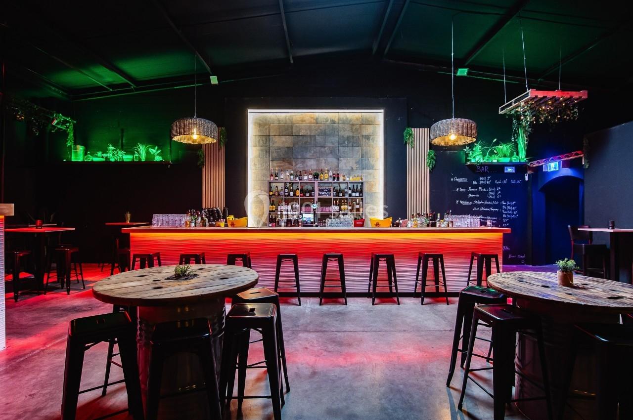 Bar moderne avec comptoir éclairé en rouge, étagères de bouteilles, tables en bois et ambiance tamisée.