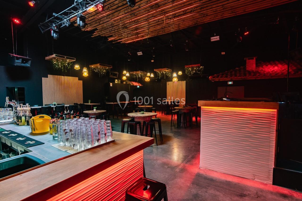 Salle de bar moderne avec éclairage tamisé, comptoir en bois, tables hautes et décorations suspendues.