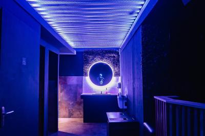 Couloir sombre avec éclairage violet, menant à un lavabo éclairé par un miroir rond lumineux.