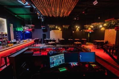 Terrasse extérieure couverte avec éclairage suspendu, séparations en bois, tables hautes et plantes décoratives.