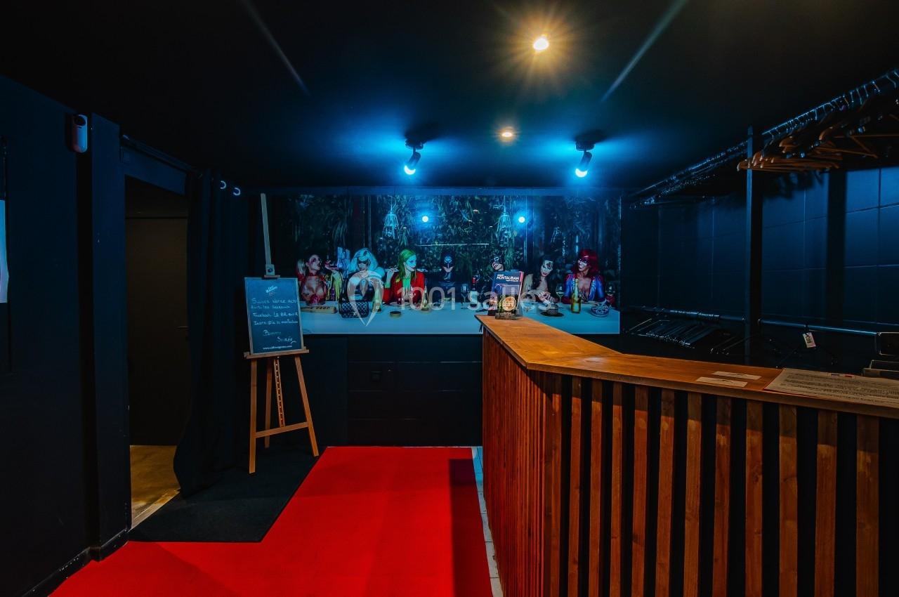 Vue d'un vestiaire avec comptoir en bois, portant des vêtements, éclairage tamisé et décoration murale colorée.