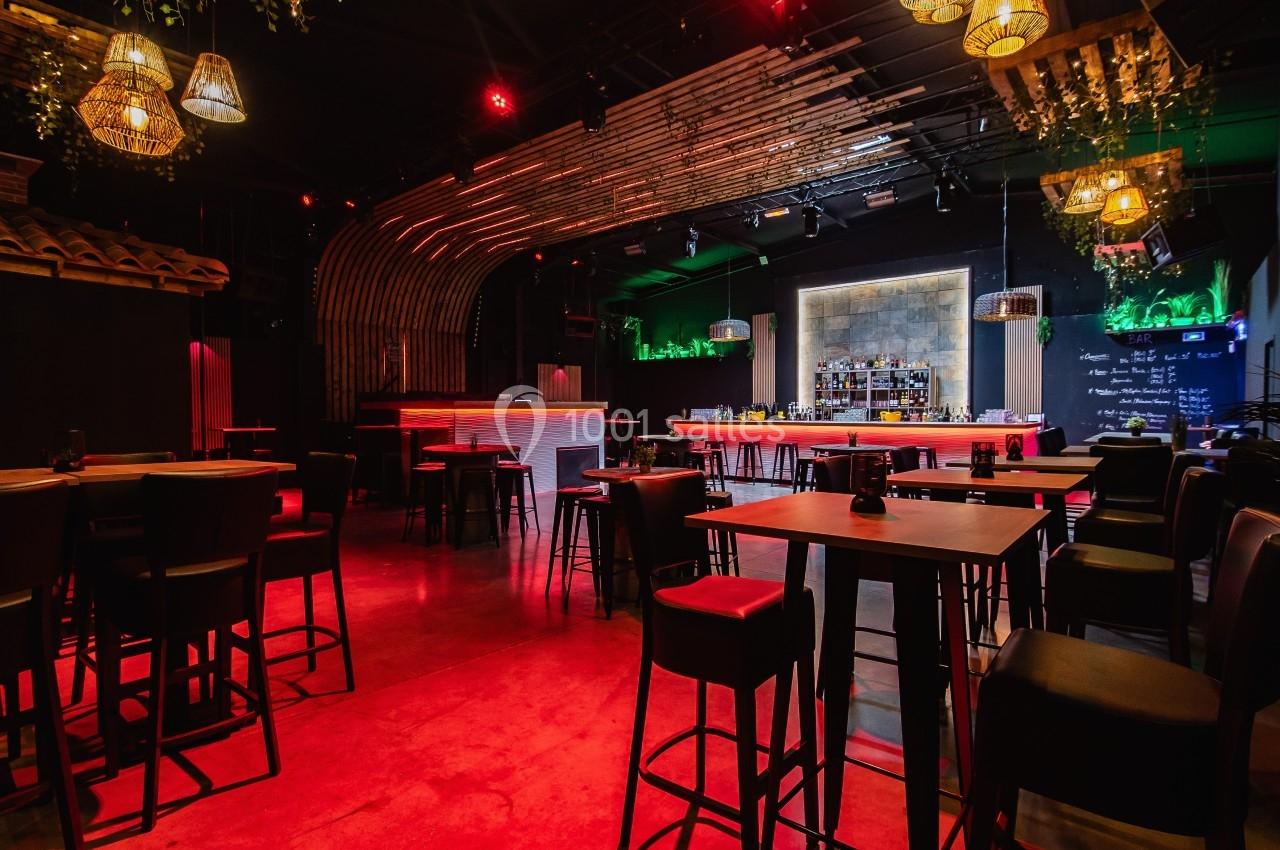 Salle de bar moderne avec éclairage tamisé rouge, tables hautes en bois et comptoir central éclairé.