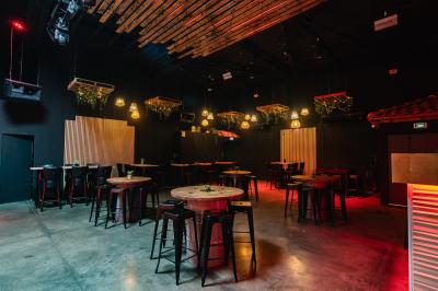 Terrasse extérieure couverte avec éclairage suspendu, séparations en bois, tables hautes et plantes décoratives.