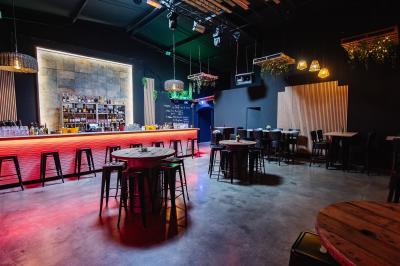 Terrasse extérieure couverte avec éclairage suspendu, séparations en bois, tables hautes et plantes décoratives.