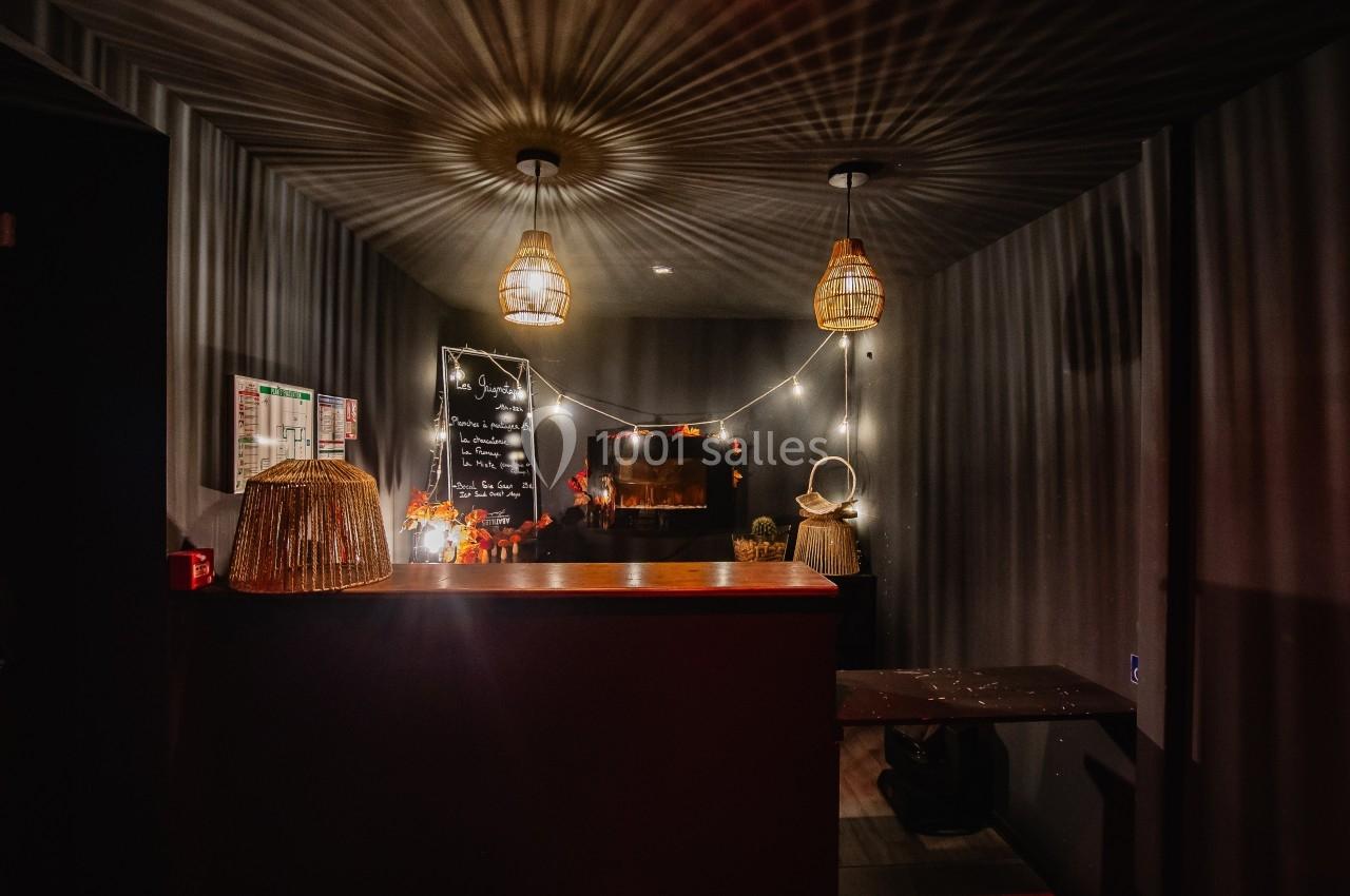 Comptoir d'accueil dans une pièce sombre, éclairée par des suspensions en osier et des guirlandes lumineuses.