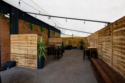 Terrasse extérieure couverte avec éclairage suspendu, séparations en bois, tables hautes et plantes décoratives.