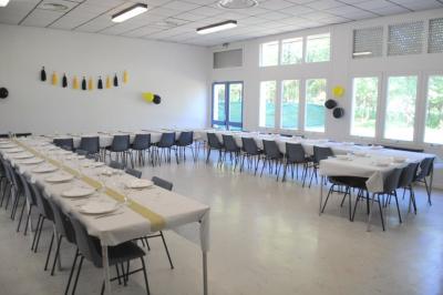 Salle décorée avec des ballons bleus, blancs et dorés, tables dressées et groupe de personnes discutant debout.
