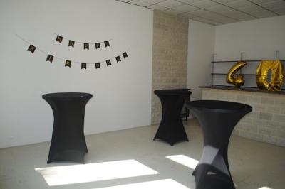 Salle décorée avec des ballons bleus, blancs et dorés, tables dressées et groupe de personnes discutant debout.